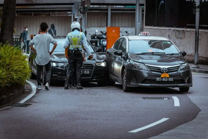 Is it illegal to drive with headphones - A traffic officer attends to a minor car accident involving a sedan and a taxi on urban street.