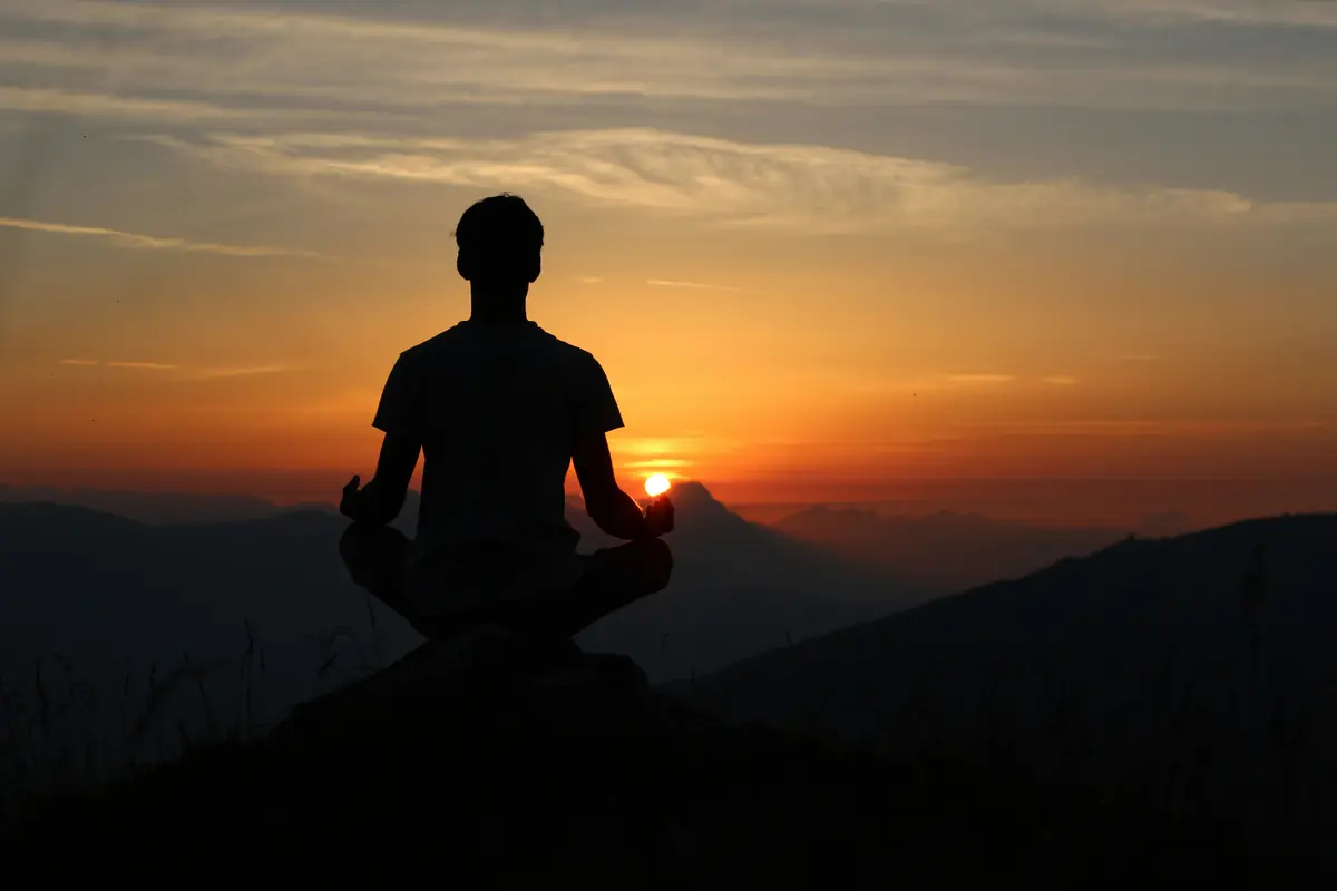 silhouette of man meditating on rock cliff during golden hour